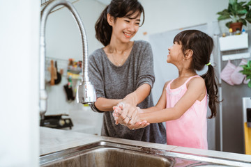 mother and daughter wash their hand together in the kitchen sink