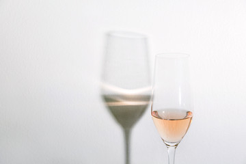 Single glass of pink rose sparkling wine in champagne flute with shadow reflection on white wall