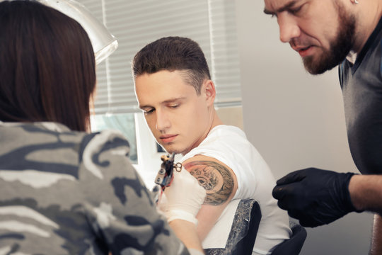 Professional tattoo master teaching young specialist in salon. Internship concept