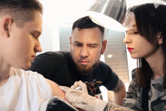 Professional tattoo master teaching young specialist in salon. Internship concept