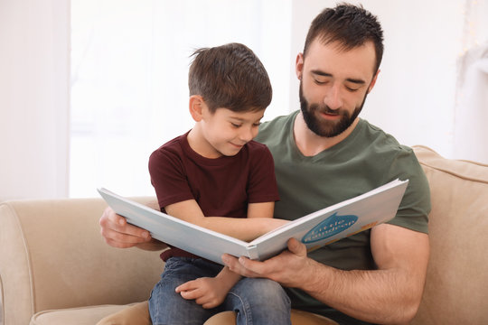 Cute little boy and his father reading book at home