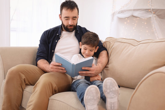 Cute little boy and his father reading book at home