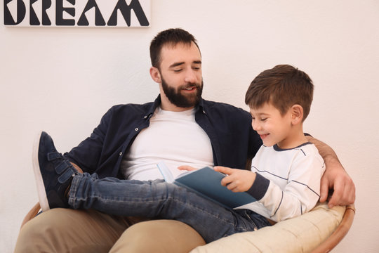 Cute little boy and his father reading book at home