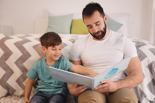 Cute little boy and his father reading book at home