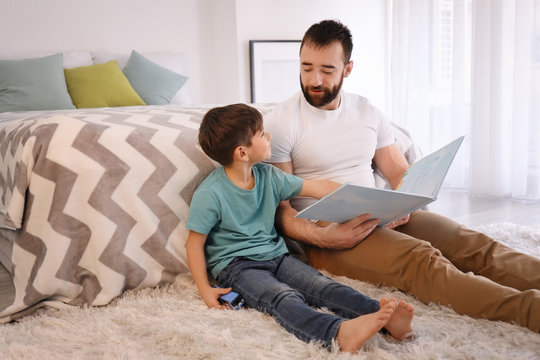 Cute little boy and his father reading book at home