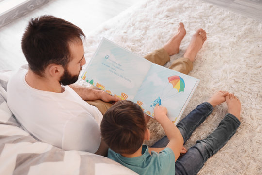 Cute little boy and his father reading book at home