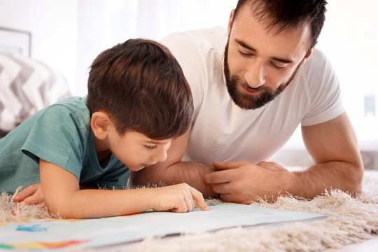 Cute little boy and his father reading book at home