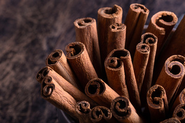 Cinnamon sticks in ceramic bowl on black rustic background with copyspace.