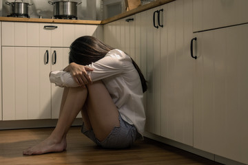 Depressed young beautiful Asian woman sitting on kitchen floor with hugging knees. Loneliness sad...