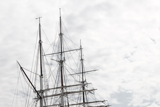 Elaborate rigging on a three mast tall ship against a gray sky, horizontal aspect