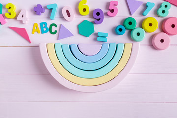Wooden toy rainbow, pastel color arc   on light pink background. Natural 
no plastic toys for creativity development. Flat lay, top view. Educational games for kindergarten, preschool kids