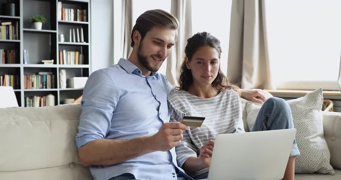 Happy young couple customers holding credit card buy products or services online using laptop. Smiling husband and wife shoppers pay doing shopping on website making e commerce secure digital payment.