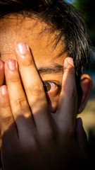 Fototapeta premium Close up view of portrait of male eyes seeing through finger gaps.