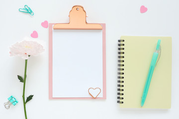 .pink clipboard, yellow notebook on a spring, pink chrysanthemum flower, blue pen, paper clips and plastic hearts..