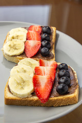 Sandwiches with fruits on a grey plate. Concept of delicious and healthy breakfast. Toasts with chocolate topping, banana, strawberry and blueberry.