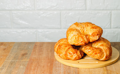Three homemade croissants are placed on a wooden tray, which is placed on a wooden table in a white brick backdrop.