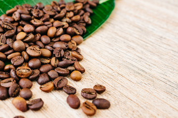 Coffee on a green leaf and scattered on a light wooden table, top view, closeup grains, place to insert text, copy space