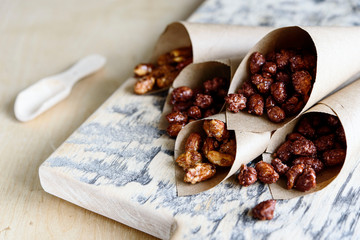 Caramelized sugared peanuts in paper envelope bags on wooden background. Selective focus