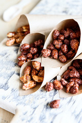 Caramelized sugared peanuts in paper envelope bags on wooden background. Selective focus
