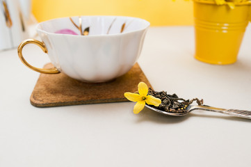 spring tea party. white porcelain mug with a gold handle and a silver spoon with tea granules and...