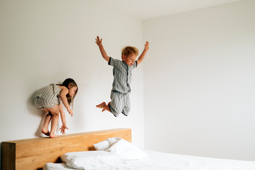 siblings playing on bed jumping on matress on a mornig daylight