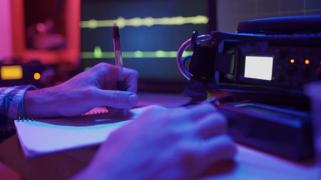 Hands take note while recording voice and sound with mixers and console in studio