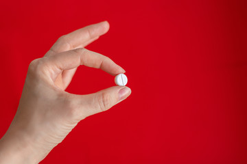 Hand holding a pill on a red background, a cure for the virus