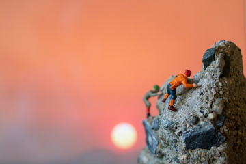Miniature people: Hikers climbing up on the rock . Sport and leisure concept.