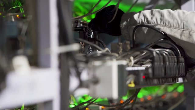 Data center diagnostics technician installs ASIC bitcoin miner on rack, connects ethernet cable. Mining equipment server service. Administrator repairs farm cryptocurrency computing cluster network.