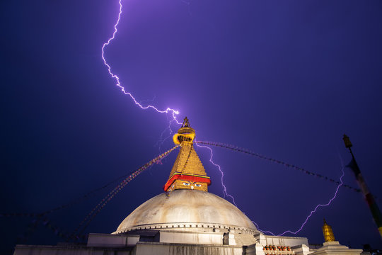A thunderstorm front over center of the Bouddnath stupa. Discharge of lightning strikes, flags and a stupa with night illumination are visible.
