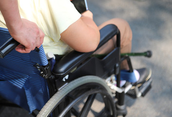 Closeup of man's  hand assisting elderly  woman  in wheelchair in sunny day. 
