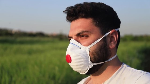 profile of yooung man wearing a mask in fornt a green field the nature, closeup