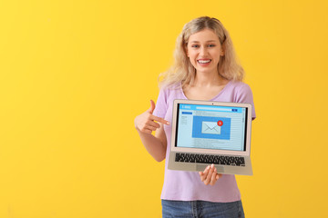 Young woman with laptop checking her e-mail on color background