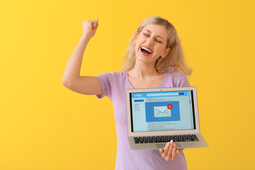 Happy young woman with laptop checking her e-mail on color background