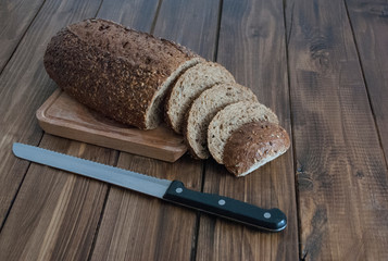 loaf of black bread with a knife on a wooden board