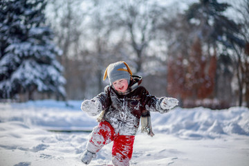 A little handsome boy in red pants and a brown sheepskin coat makes his way through the snowdrifts...