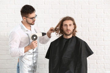 Young hairdresser working with client against white brick background