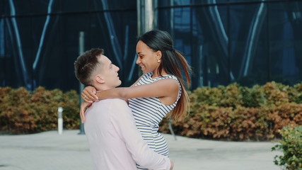 Smiling multiracial couple having fun spinning around on the street. A big office building is in the background.