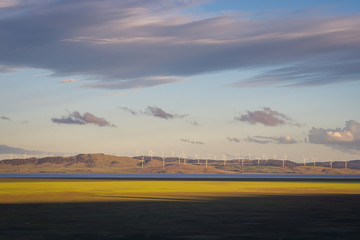 Golden yellow sunlight shining on a vast open plain with a wind farm and mountains in the...