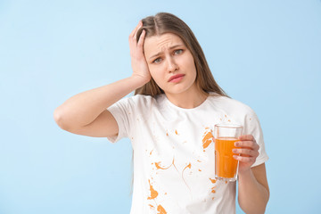Troubled woman in dirty clothes drinking juice on color background