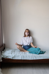 Rest at home during quarantine. Young beautiful woman is sitting on the bed. Meditation at home.