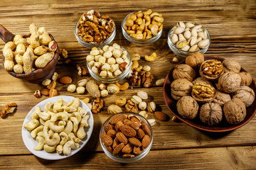 Assortment of nuts on wooden table. Almond, hazelnut, pistachio, peanut, walnut and cashew in small bowls. Healthy eating concept