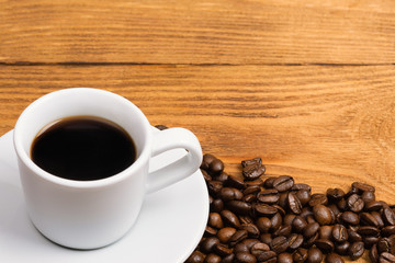 Freshly made coffee in a white cup surrounded by coffee beans on a wooden table. Fresh roasted coffee.