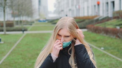 Young female feeling saved by putting on face medical mask. She standing in the city center. Coronavirus pandemic concept.