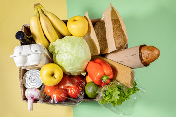 Top view of cardboard box with fresh food products on green-yellow background. Safe delivery. Top...