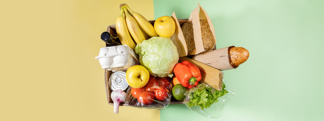 Top view of cardboard box with food products on color green-yellow background. Safe delivery....