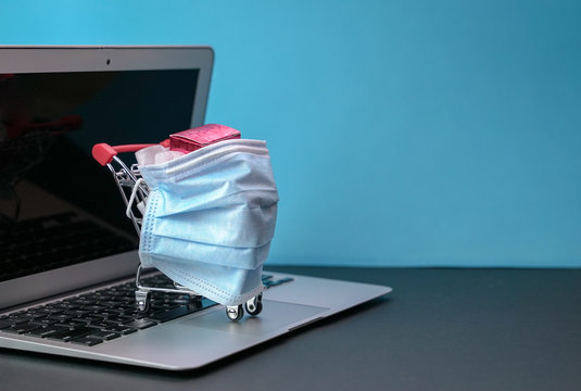 Shopping Trolley Or Cart Wrapped With Medical Face Mask Stand On Top Of Computer Laptop.