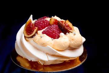 Close up of dessert Pavlova with raspberries and figs against a dark background