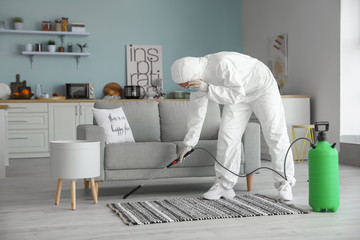 Worker in biohazard suit disinfecting house