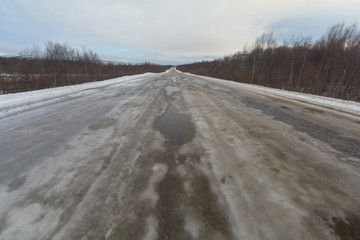 The dirt road is covered with ice .The sky is covered with clouds.